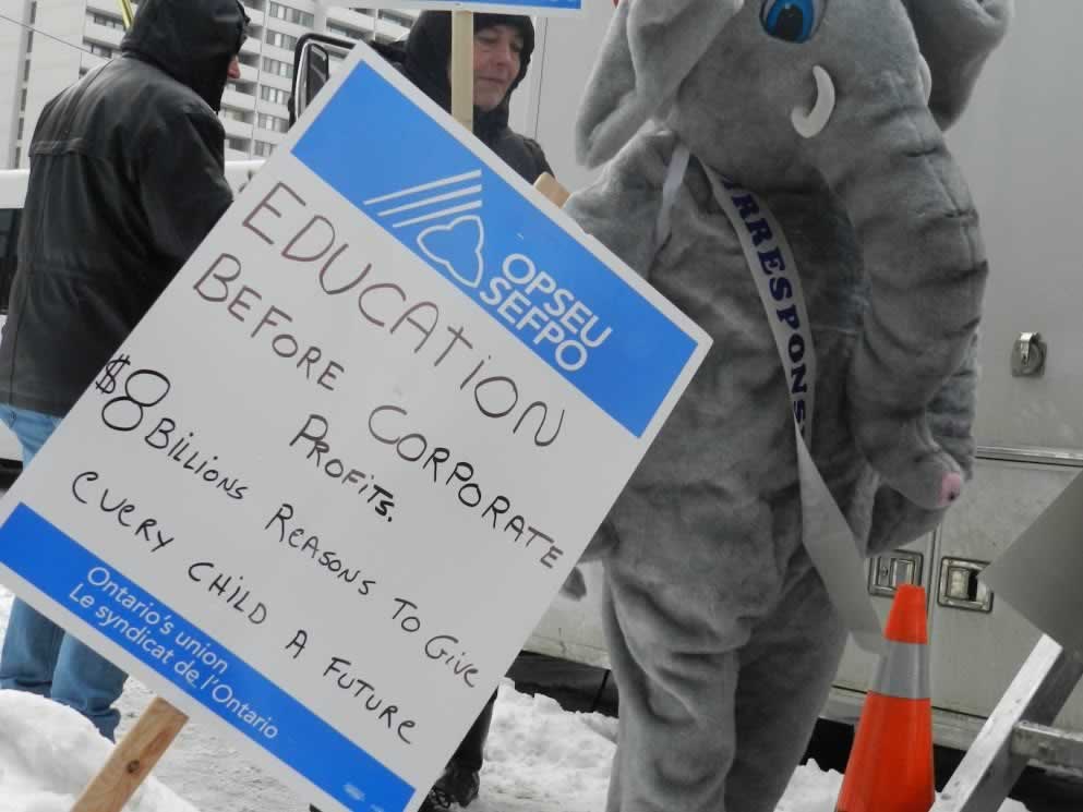 Person in elephant costume standing next to sign that says: Education before corporate profits. $8 billions reasons to give every child a future