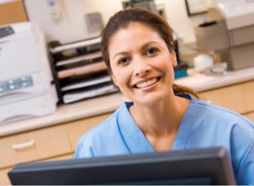 A young smiling woman in blue scrubs sitting in front of a computer