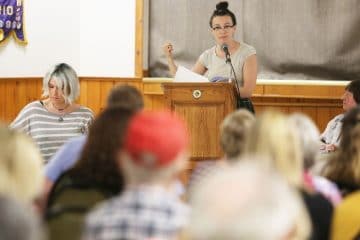 Woman at a podium speaking to a group of people.