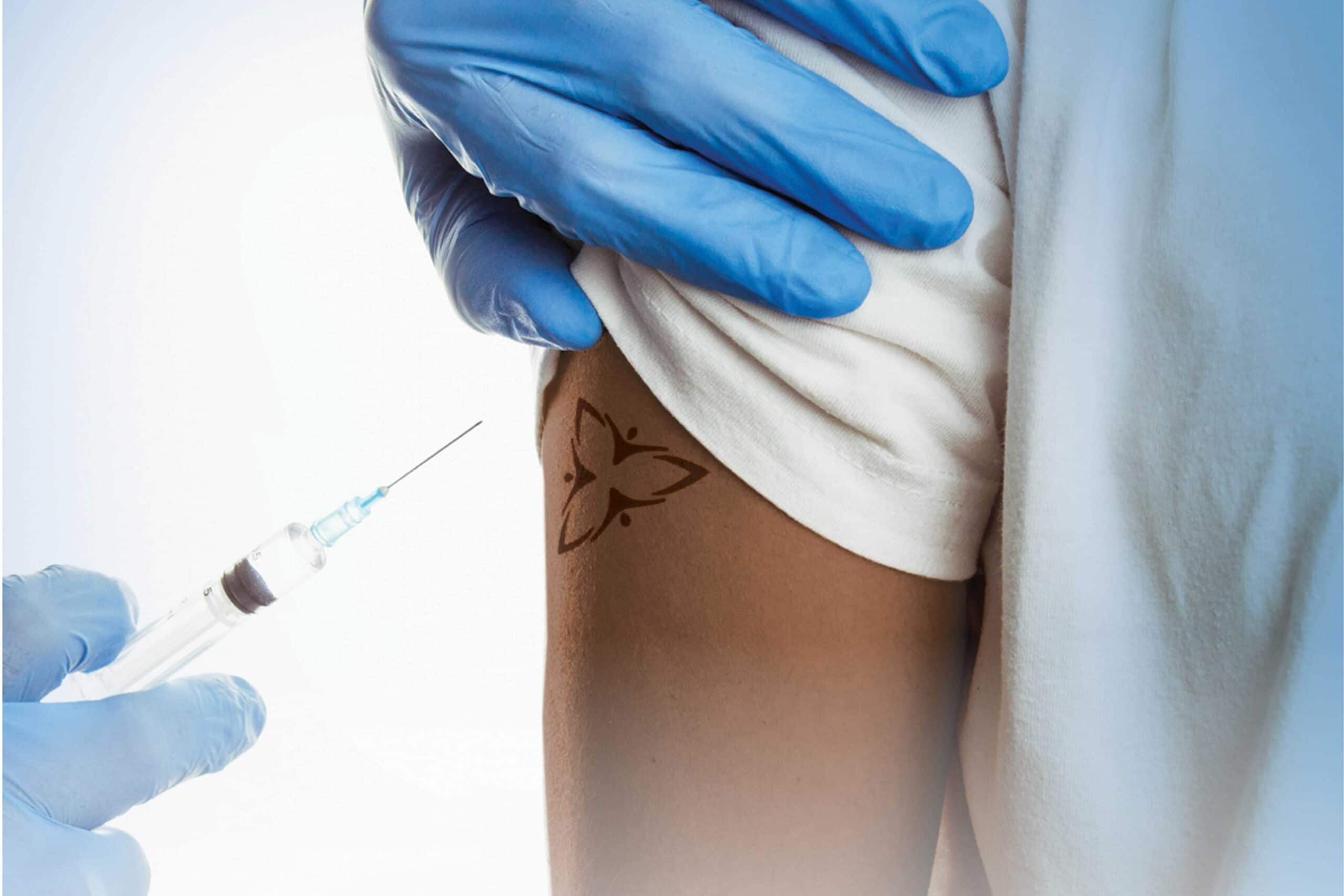Upper arm with Ontario trillium logo with gloved hand holding vaccine needle beside arm.